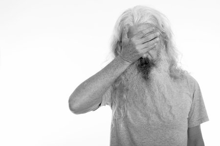 Studio shot of senior bearded man looking tired while covering eyes