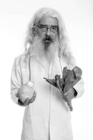 Studio shot of senior bearded man doctor holding cabbage and vegetablesの写真素材