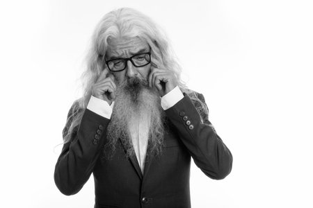 Studio shot of sad senior bearded businessman crying with both hands while wearing eyeglasses