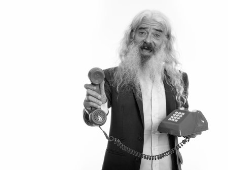Studio shot of happy senior bearded businessman smiling while giving old telephone