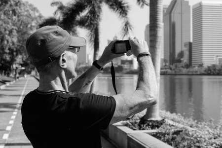 Senior tourist man wearing cap while taking pictures at peaceful park in Bangkok Thailandの写真素材