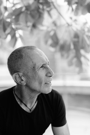 Profile view of bald senior tourist man thinking and relaxing under the tree in the cityの写真素材