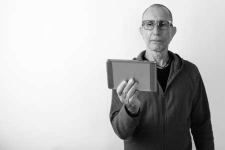 Studio shot of bald senior man using digital tablet while wearing eyeglasses against white backgroundの写真素材