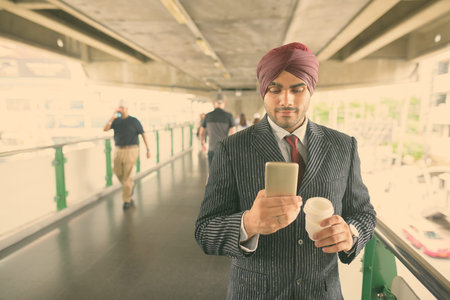 Young handsome Indian Sikh businessman wearing turban while exploring the city