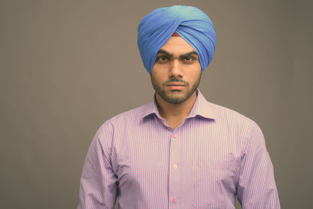 Young handsome Indian businessman wearing turban against gray background