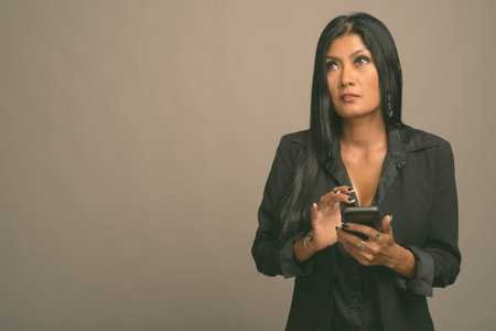 Mature beautiful Asian businesswoman against gray backgroundの写真素材