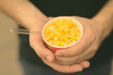 Hands of young man holding cup of deliciously steamed sweet cornの写真素材
