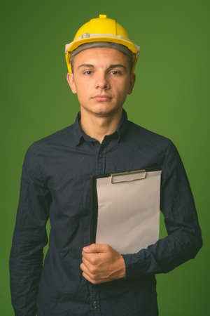 Young handsome businessman with hardhat against green backgroundの写真素材