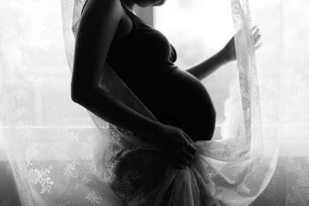 Mother loving her baby in silhouette by the windowの写真素材