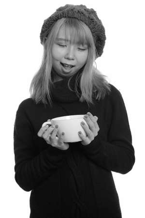 Young happy Asian woman smiling while holding and looking at coffee cupの写真素材