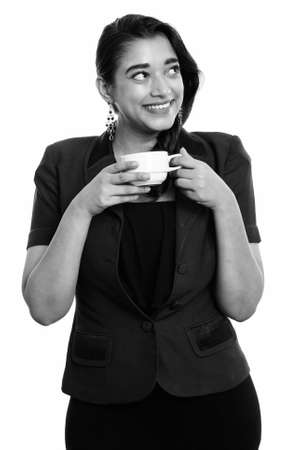 Young happy Indian businesswoman smiling while thinking and holding coffee cupの写真素材