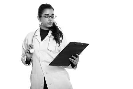 Studio shot of young beautiful Indian woman doctor reading on clipboardの写真素材