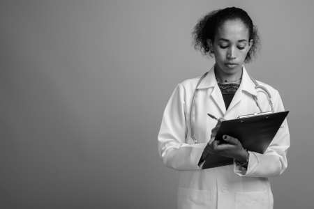 Young beautiful African woman doctor against gray backgroundの写真素材