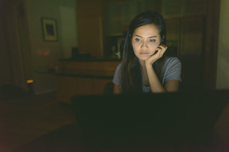 Young beautiful Asian woman using laptop in the dark living room