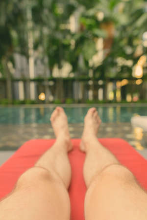 Feet of young handsome man relaxing by swimming pool in hotel at Kuala Lumpur, Malaysiaの写真素材
