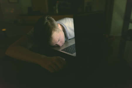 Young handsome man using laptop in the dark living roomの写真素材