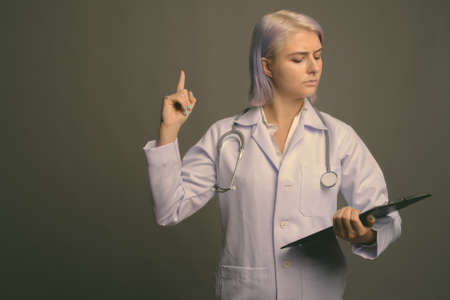 Young beautiful woman doctor with short colorful hair against gray backgroundの写真素材