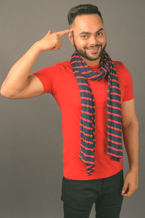 Young bearded Indian man against gray background