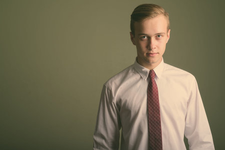 Young handsome businessman with blond hair against colored background