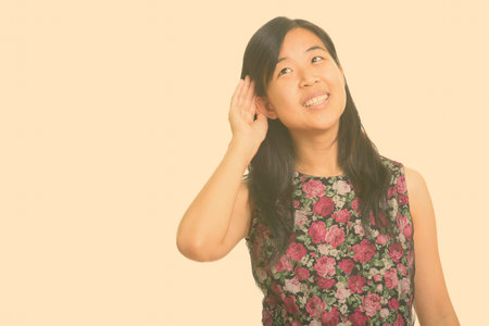 Portrait of happy young beautiful Asian businesswoman listening