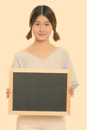 Studio shot of young beautiful Asian woman holding blank blackboardの写真素材