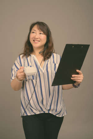 Mature beautiful Asian businesswoman against gray backgroundの写真素材