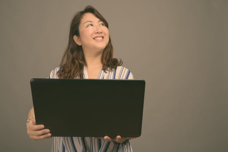 Mature beautiful Asian businesswoman against gray background