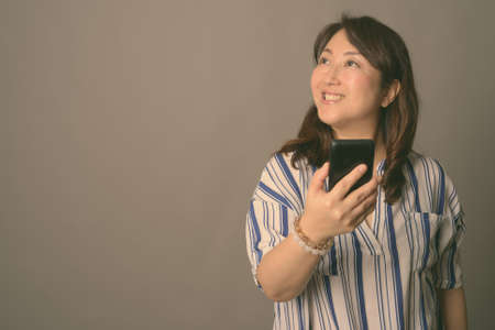 Mature beautiful Asian businesswoman against gray backgroundの写真素材