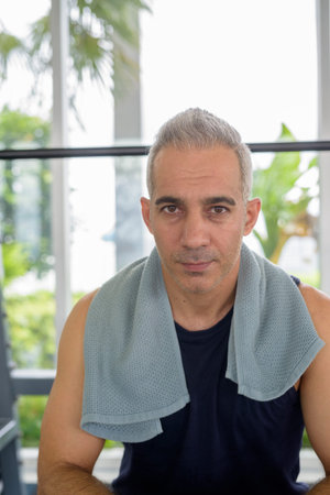 Portrait of mature handsome Persian man sitting at the gym