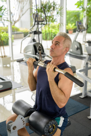 Mature handsome Persian man exercising with pull down machine at the gym