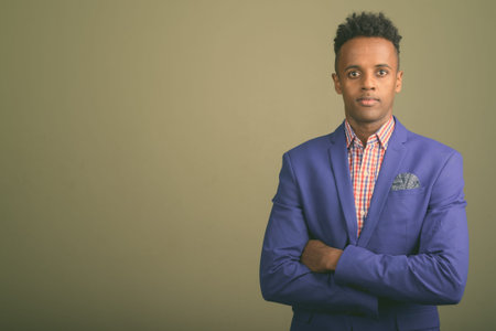 Young handsome African businessman wearing suit against colored background