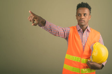Young handsome African man construction worker against colored background