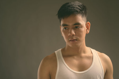 Young handsome Asian man wearing tank top against gray background