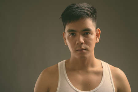 Young handsome Asian man wearing tank top against gray backgroundの写真素材