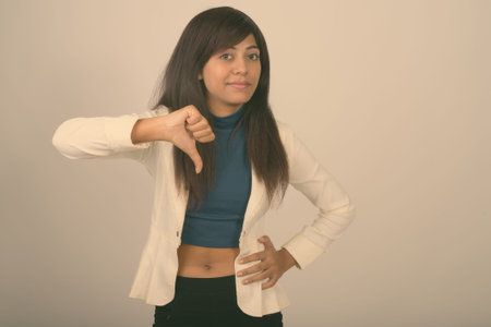 Studio shot of young Persian businesswoman giving thumb down against gray background