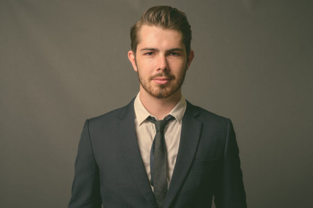 Young handsome bearded businessman against gray background