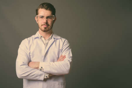 Young handsome bearded man doctor wearing protective glasses against gray backgroundの写真素材