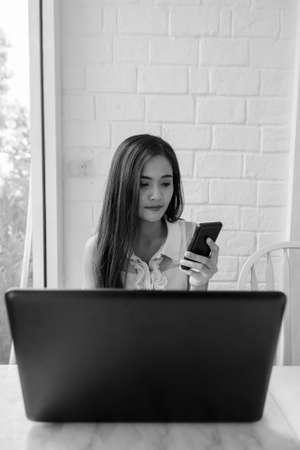 Young beautiful Asian woman using phone and laptop computerの写真素材