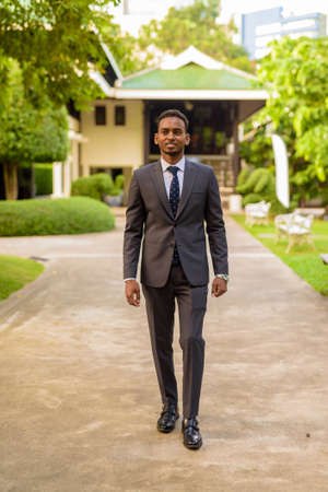 Full length shot of young handsome African businessman walking at parkの写真素材