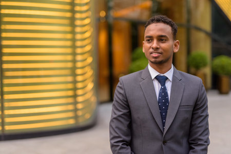 Portrait of young handsome African businessman outdoors thinking