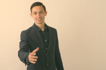 Studio shot of young happy businessman smiling while giving handshake against white background
