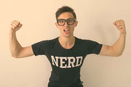 Studio shot of young nerd man flexing both arms while wearing eyeglasses against white backgroundの写真素材