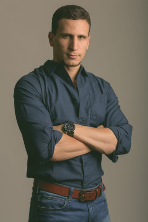 Studio shot of young muscular Persian man with arms crossed against gray background