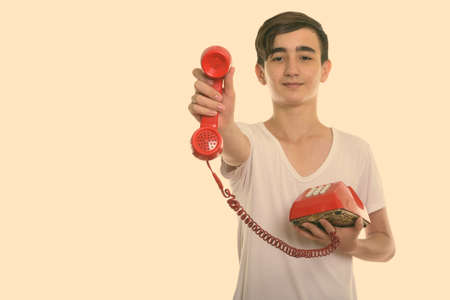 Studio shot of young handsome Persian teenage boy giving old telephoneの写真素材