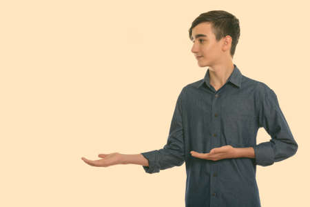 Profile view of young handsome Persian teenage boy showing somethingの写真素材
