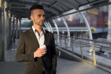 Businessman outdoors in city holding coffee cup while thinkingの写真素材