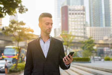 Portrait of handsome young businessman outdoors in city using phoneの写真素材