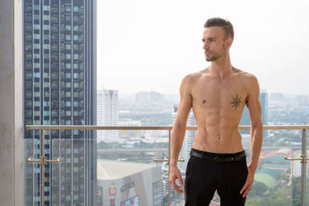 Portrait of handsome young man shirtless outdoors at rooftop in cityの写真素材