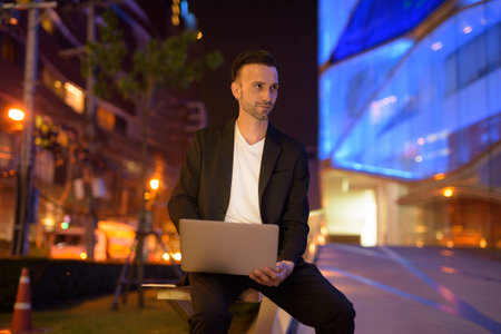 Portrait of young businessman using laptop against a city by night