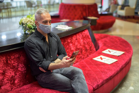 Portrait of man sitting while social distancing and using mobile phone